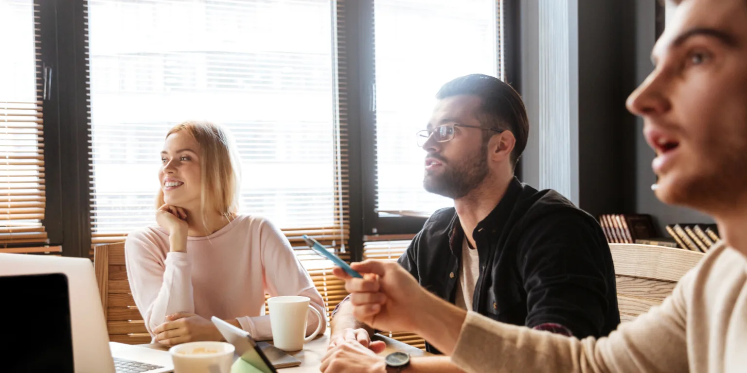 A small team meeting around a table with laptops and coffee, deep in conversation