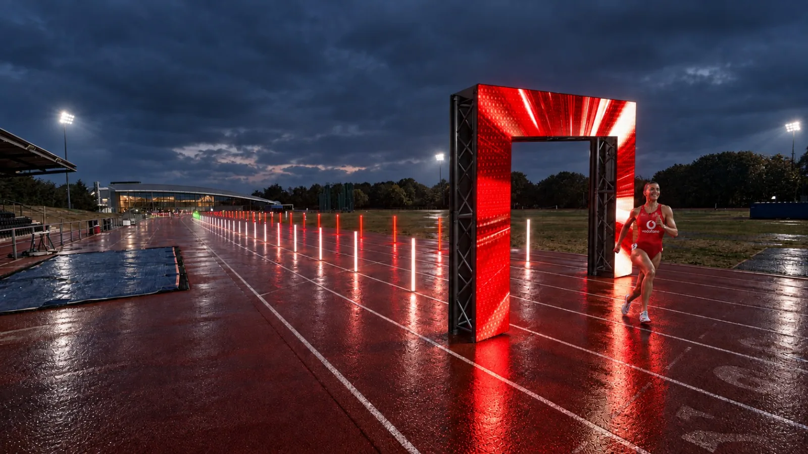 A runner sprinting through a lit LED archway on a running track at night, lined with glowing markers